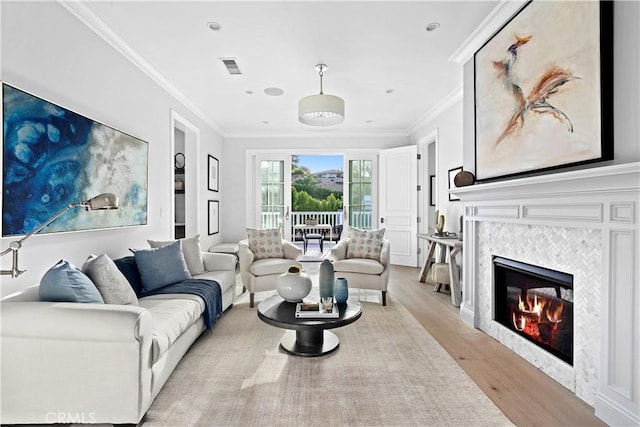 living area with light wood finished floors, visible vents, crown molding, and a tile fireplace