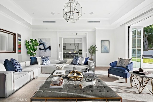 living area with a tray ceiling, visible vents, and ornamental molding