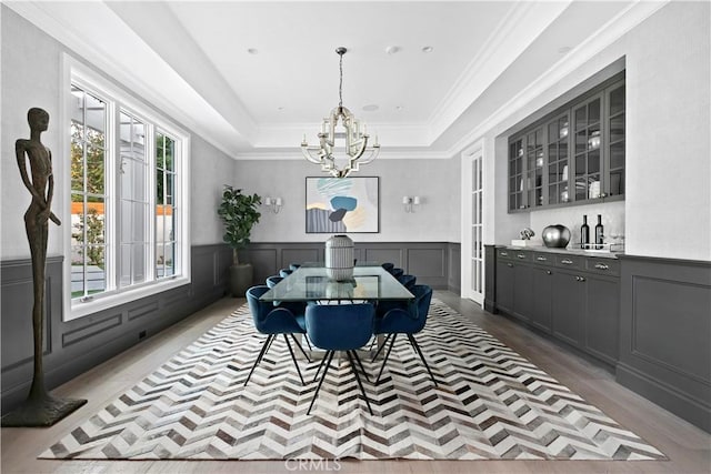 dining room featuring ornamental molding, a chandelier, a raised ceiling, a wainscoted wall, and a decorative wall
