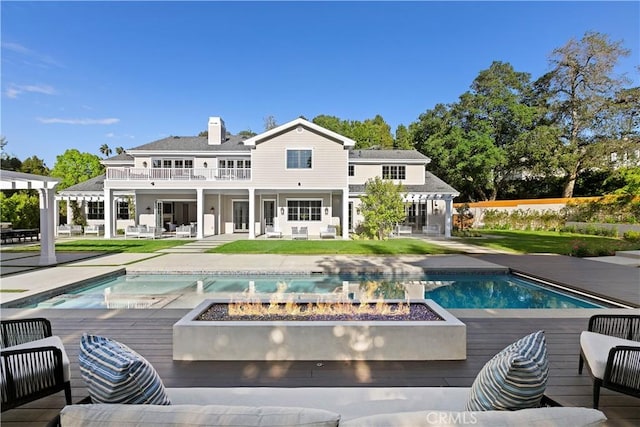 back of house with a balcony, an outdoor pool, a chimney, a jacuzzi, and an outdoor living space with a fire pit