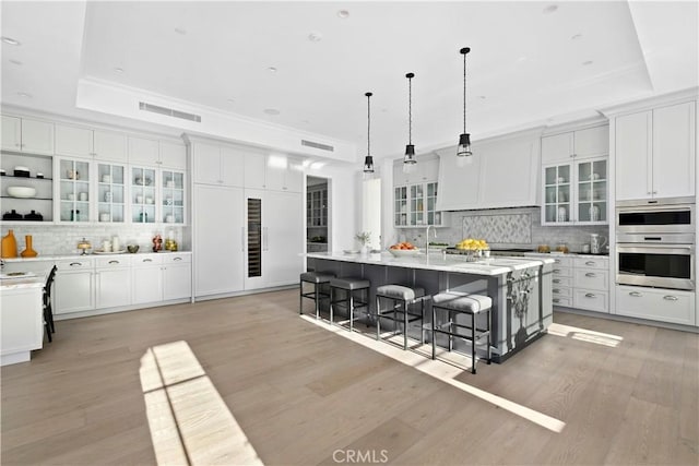 kitchen with a tray ceiling, double oven, tasteful backsplash, a kitchen bar, and a large island