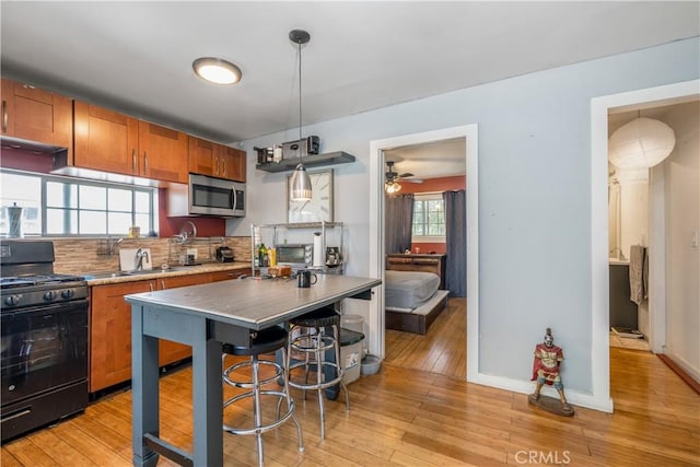 1361 W Vernon Ave, Los Angeles, CA 90037 - kitchen featuring decorative backsplash, light wood finished floors, black range with gas stovetop, stainless steel microwave, and brown cabinets