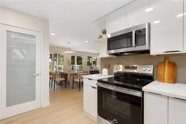 2405 Via Mariposa W Unit 1B, Laguna Woods, CA 92637 - kitchen featuring stainless steel appliances, white cabinetry, light countertops, backsplash, and light wood-type flooring