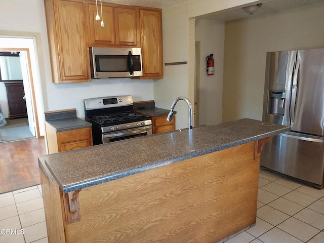 1420 S Butler Ave, Compton, CA 90221 - kitchen featuring appliances with stainless steel finishes, light tile patterned floors, a breakfast bar, brown cabinets, and an island with sink