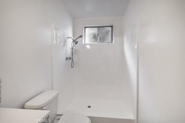 bathroom with toilet, vanity, and tiled shower