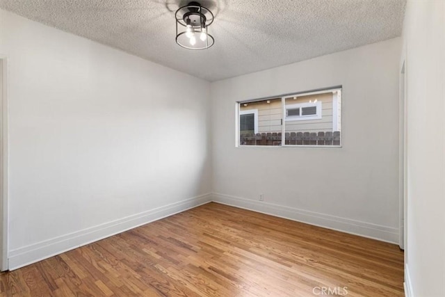 spare room featuring a textured ceiling, baseboards, and light wood-type flooring