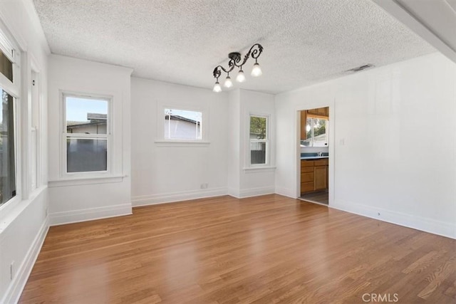unfurnished dining area featuring baseboards, a textured ceiling, visible vents, and light wood finished floors