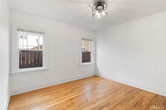 empty room with a wealth of natural light, light wood-type flooring, ceiling fan, and baseboards