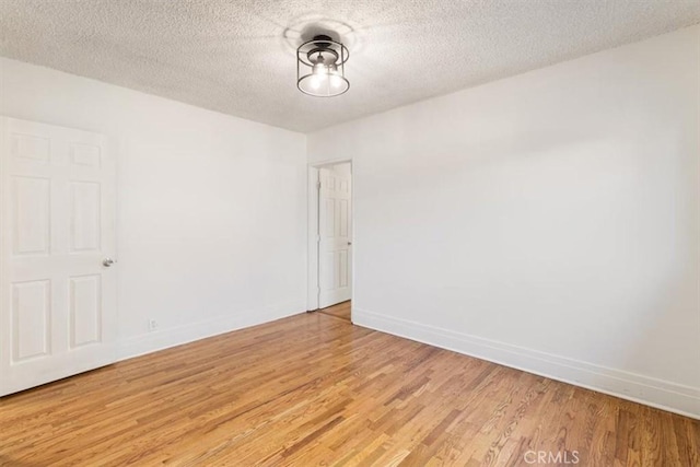 unfurnished room featuring baseboards, a textured ceiling, and light wood finished floors