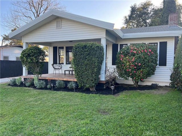 view of front of house featuring a front lawn, a chimney, covered porch, and fence