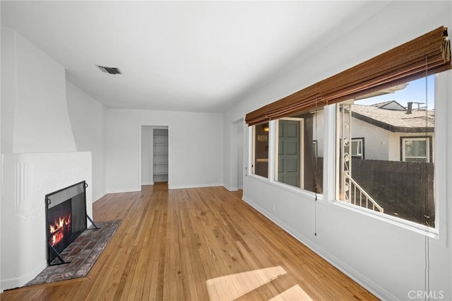 unfurnished living room with a large fireplace, visible vents, baseboards, and hardwood / wood-style floors