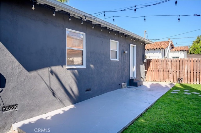 view of side of home with crawl space, stucco siding, a lawn, a patio, and fence