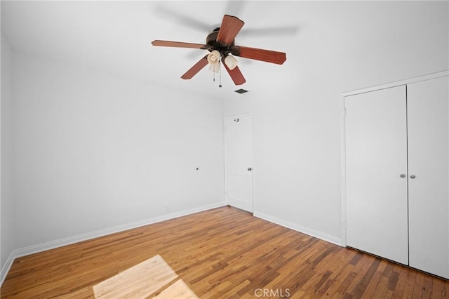 unfurnished bedroom with a closet, baseboards, a ceiling fan, visible vents, and wood finished floors