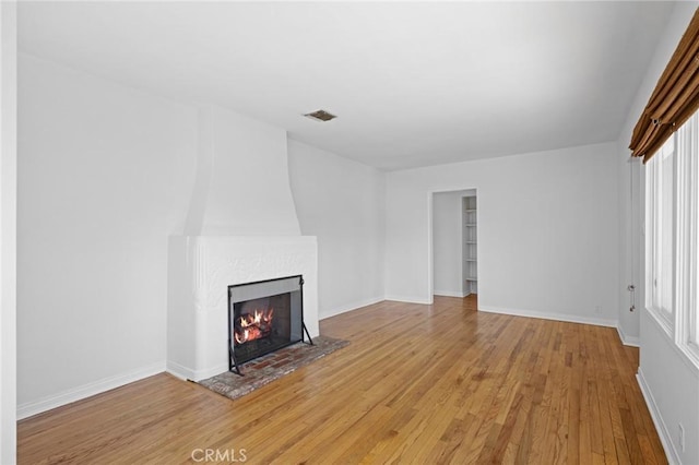 unfurnished living room with baseboards, light wood finished floors, a fireplace, and visible vents