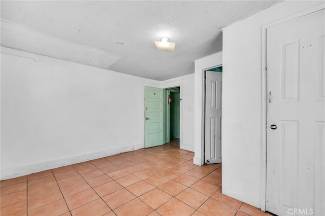 empty room featuring light tile patterned flooring, a textured ceiling, and baseboards
