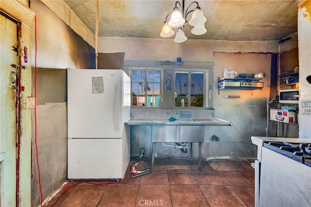 kitchen with freestanding refrigerator, gas range, and an inviting chandelier