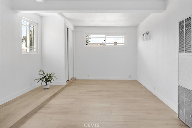 spare room featuring a heating unit, plenty of natural light, baseboards, and light wood finished floors