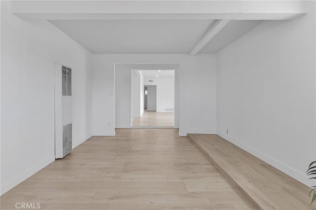 spare room featuring baseboards, beamed ceiling, light wood finished floors, and a heating unit