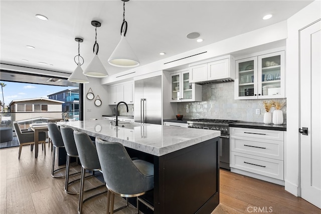 kitchen featuring a sink, high end appliances, decorative backsplash, glass insert cabinets, and white cabinetry