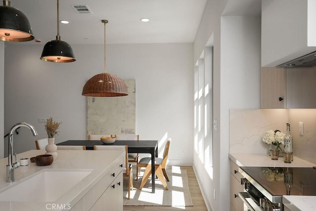 kitchen featuring light wood-style flooring, light countertops, decorative light fixtures, visible vents, and a sink