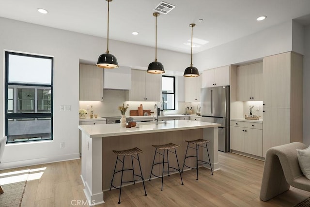 kitchen featuring visible vents, a sink, freestanding refrigerator, a kitchen bar, and light wood-style flooring