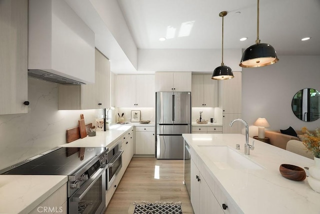 kitchen with decorative light fixtures, a sink, light wood finished floors, stainless steel appliances, and light stone counters