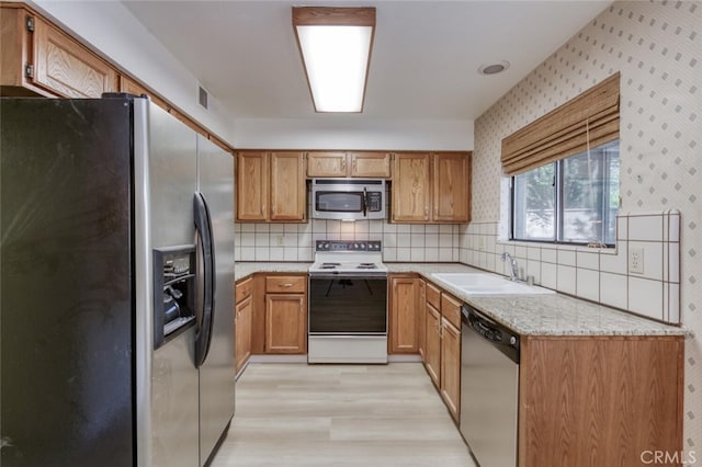 4837 N Hulbert Ave, Fresno, CA 93705 - kitchen with stainless steel appliances, light wood finished floors, wallpapered walls, backsplash, and brown cabinetry