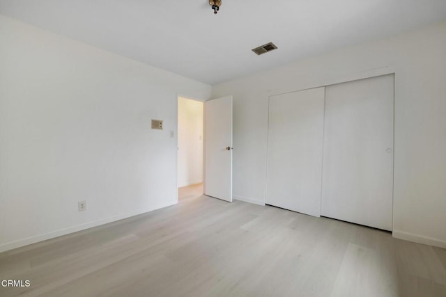 unfurnished bedroom featuring wood finished floors, a closet, baseboards, and visible vents