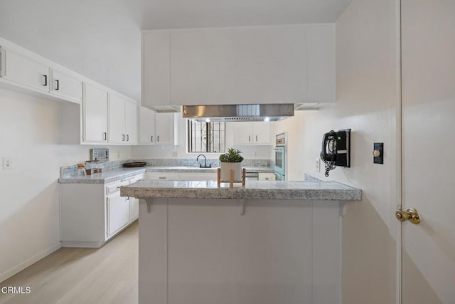 kitchen featuring white oven, light wood finished floors, white cabinetry, a breakfast bar area, and a peninsula