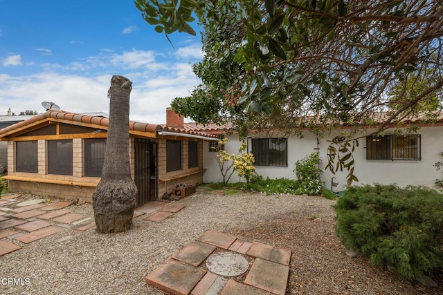 back of house featuring stucco siding, a chimney, and a tile roof