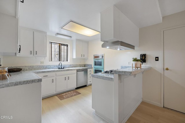 kitchen featuring light countertops, a peninsula, stainless steel dishwasher, light wood-type flooring, and white cabinets