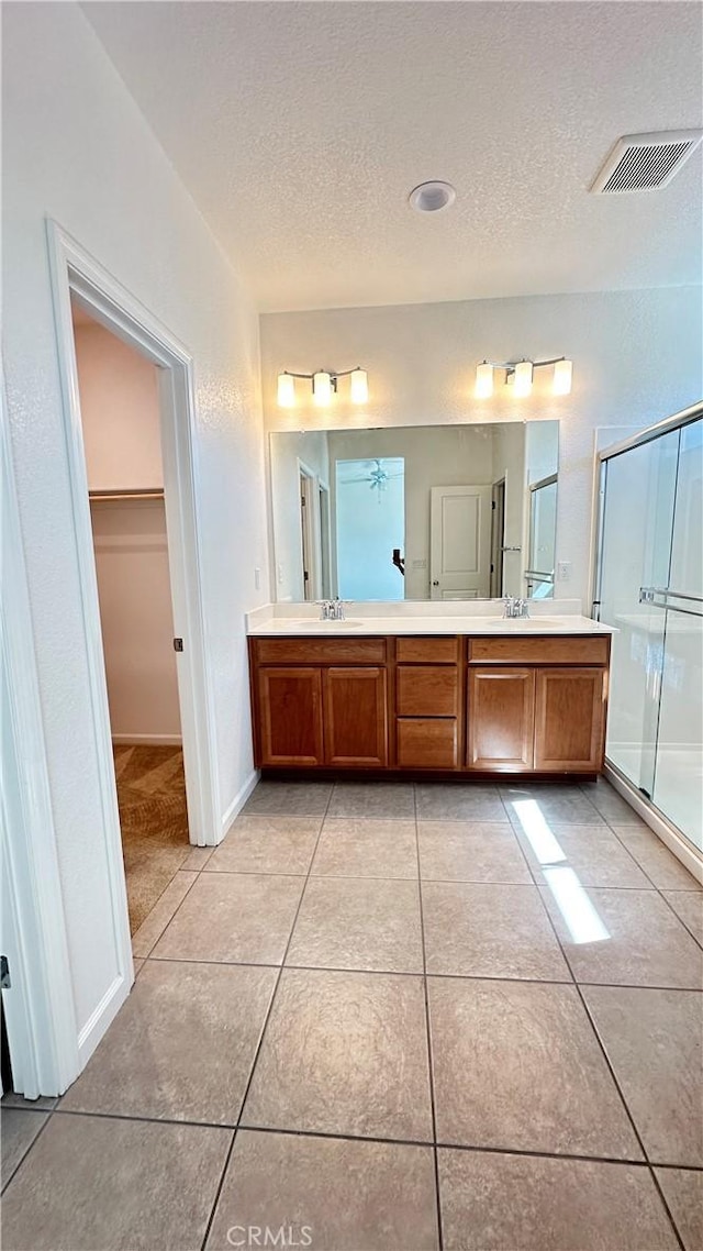 bathroom featuring tile patterned flooring, a textured ceiling, a stall shower, visible vents, and double vanity