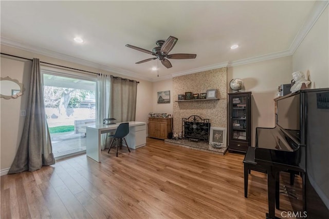 office space featuring a ceiling fan, ornamental molding, light wood-style flooring, and a large fireplace