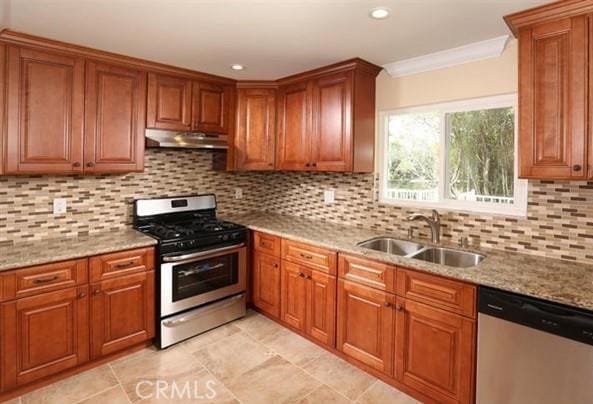 kitchen with brown cabinetry, a sink, light stone counters, ornamental molding, and stainless steel appliances