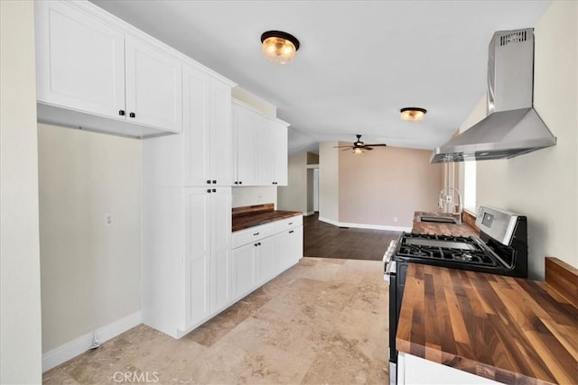 kitchen with wall chimney range hood, ceiling fan, butcher block countertops, and stainless steel gas stove