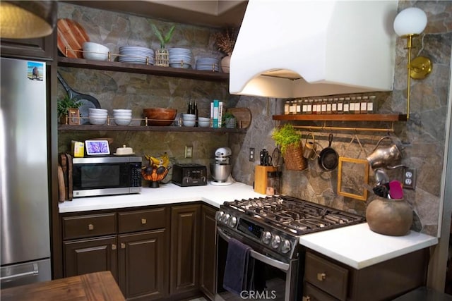 kitchen with dark brown cabinets, ventilation hood, appliances with stainless steel finishes, and open shelves