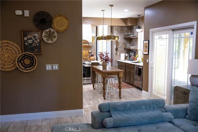kitchen with light countertops, stainless steel appliances, a sink, decorative light fixtures, and open floor plan