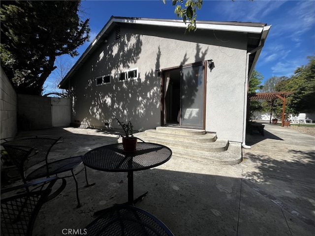 rear view of property featuring a pergola, a patio, entry steps, and stucco siding