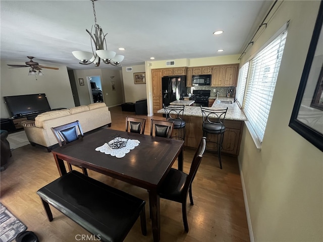 dining space featuring baseboards, ceiling fan with notable chandelier, wood finished floors, and visible vents