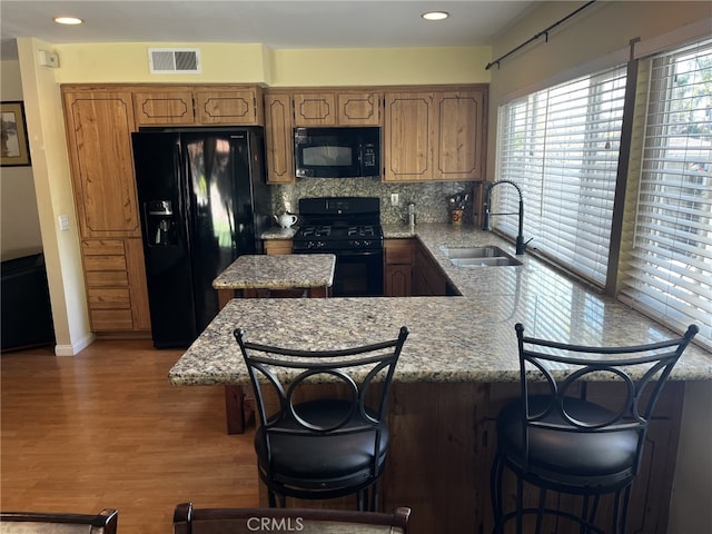 kitchen featuring a sink, a peninsula, wood finished floors, visible vents, and black appliances