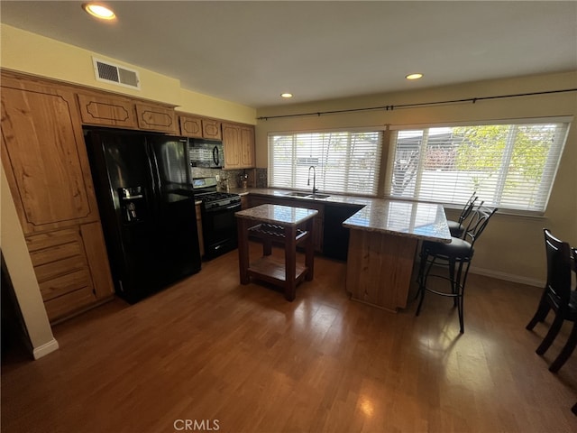 kitchen with plenty of natural light, black appliances, wood finished floors, and visible vents