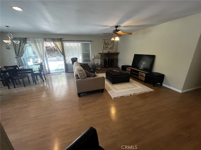 living room with a brick fireplace, a ceiling fan, baseboards, recessed lighting, and wood finished floors