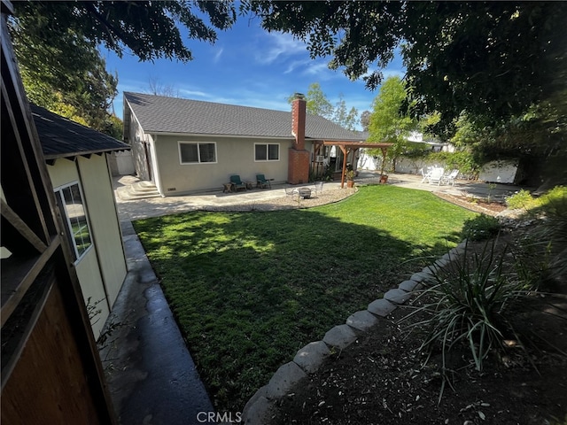 rear view of property with a lawn, a patio area, stucco siding, and a chimney