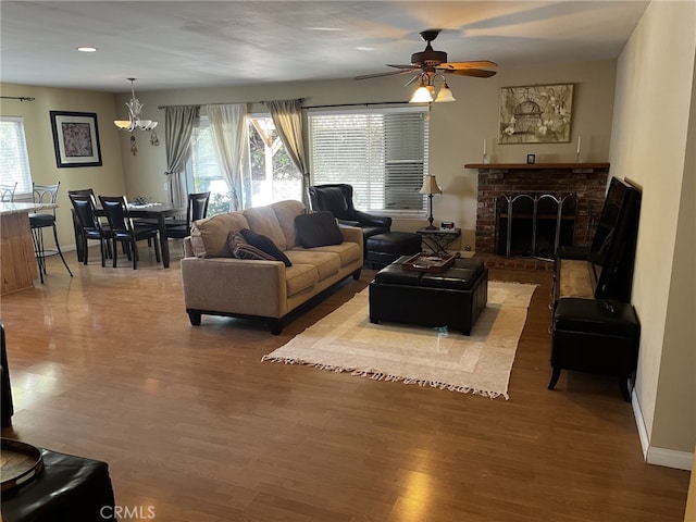 living room with baseboards, a fireplace, ceiling fan with notable chandelier, and wood finished floors