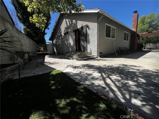 rear view of property featuring a patio, fence, a chimney, and stucco siding
