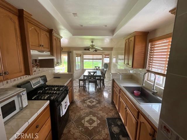 kitchen with under cabinet range hood, gas stove, a raised ceiling, a sink, and white microwave