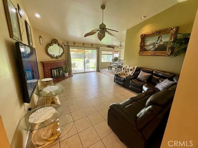 living room with light tile patterned flooring, lofted ceiling, a ceiling fan, and a brick fireplace