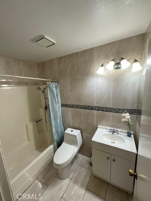 bathroom featuring toilet, vanity, tile walls, and shower / tub combo with curtain