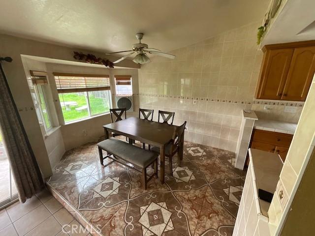 dining room with tile patterned floors, ceiling fan, and tile walls