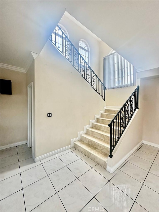stairway featuring tile patterned floors, crown molding, a high ceiling, and baseboards